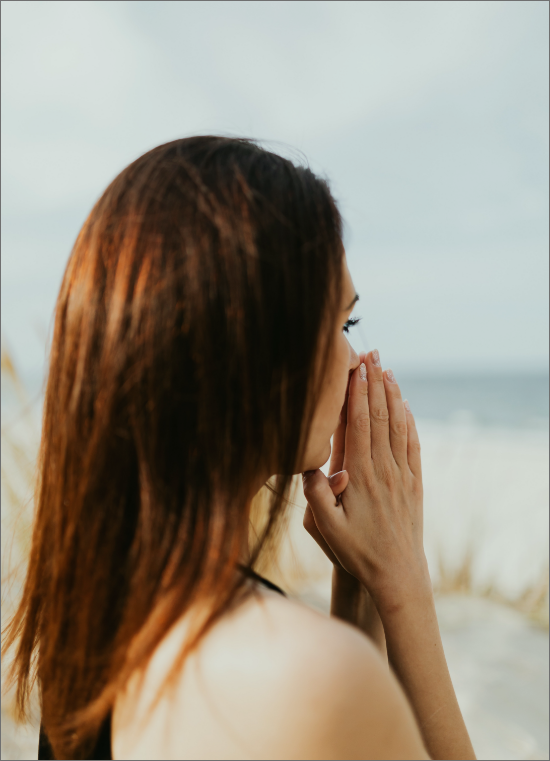 woman with long hair with back to camera, looking out to sea